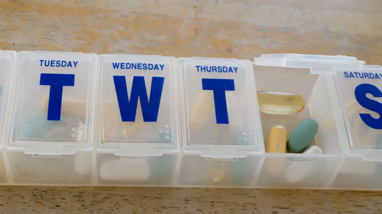 Close up on a medical prescription pill box organizer full of vitamins and health supplements with a glass of water