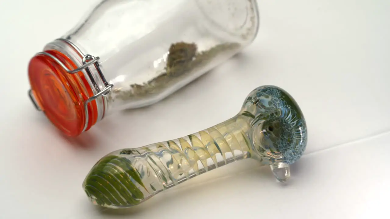 A colorful glass pipe sits next to a clear sealed bottle containing marijuana grounds