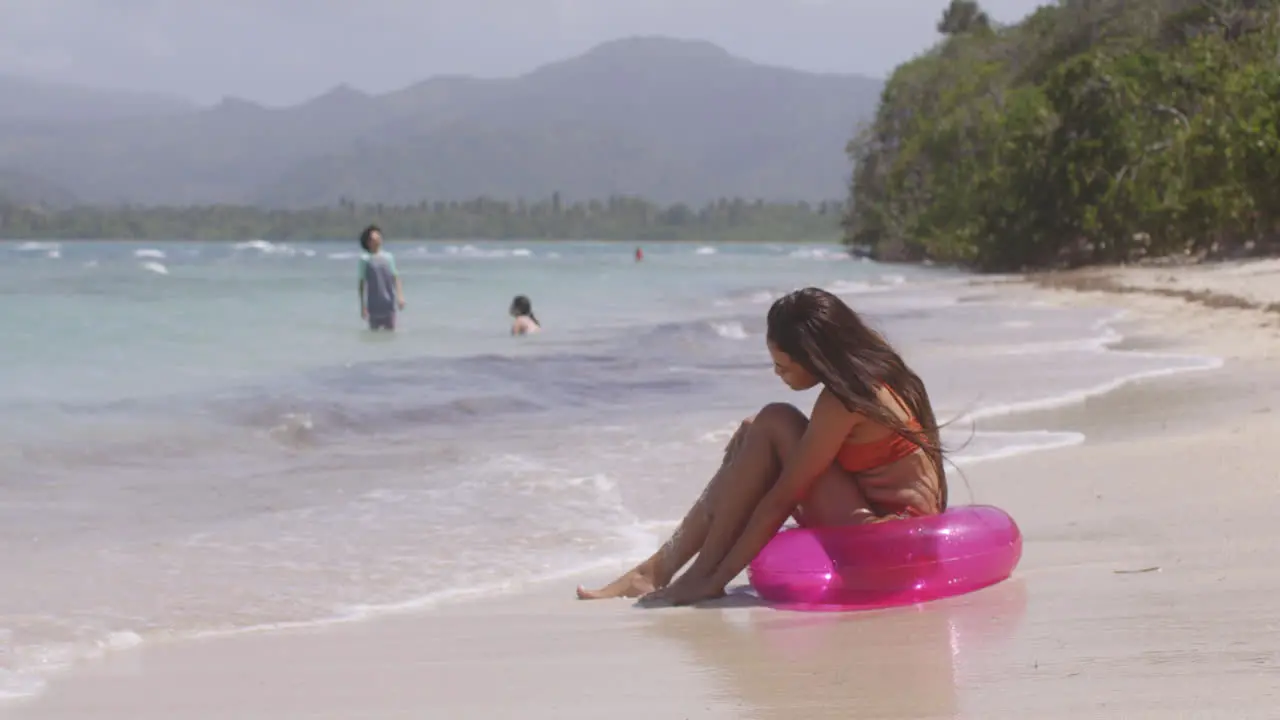 Latina Girl Enjoys Playing with Sand and Water Sitting on Tropical Island Beach in Inflatable Ring