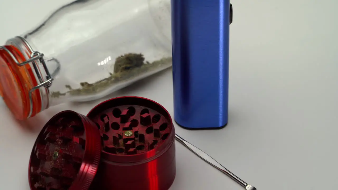 Tight shot panning across a metal scoop grinder vaporizer and sealed transparent jar of marijuana grounds