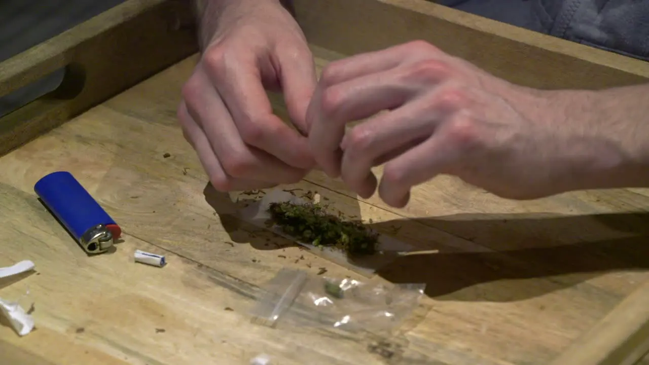 a man topping his tobacco with a lot of marijuana on a wooden tray at his home