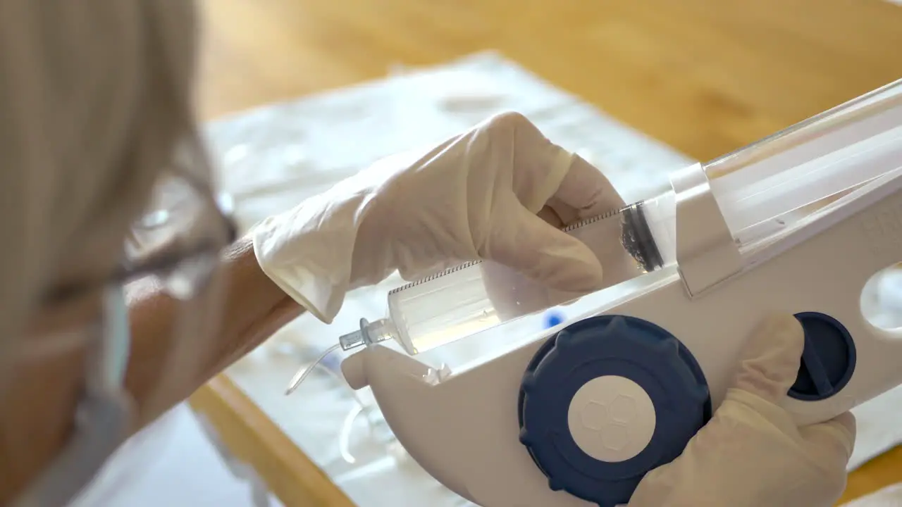 Middle aged woman medical patient wearing a face mask and sterile gloves preparing a large syringe of medicine solution for her at home infusion treatment