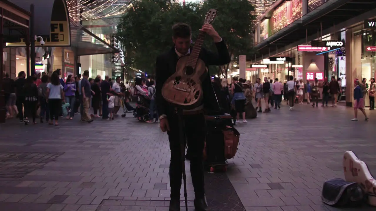 Patreons walk the street of downtown Sydney Australia during the Christmas holidays as a man plays guitar for money