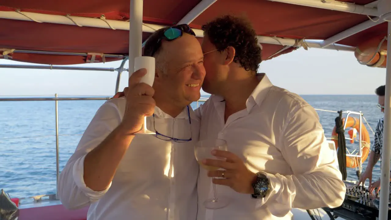 Happy guys cheers and talk on a catamaran wedding party