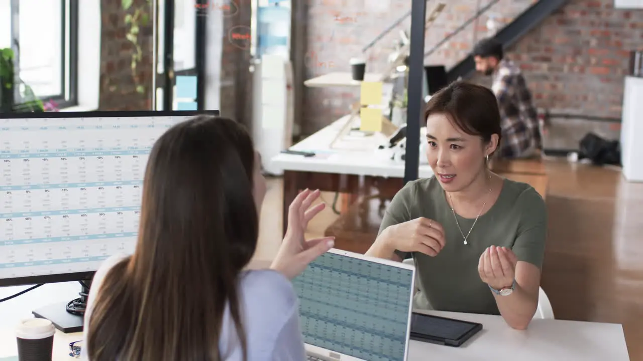 Asian woman in a green top discusses business with a young Caucasian woman across a computer monitor