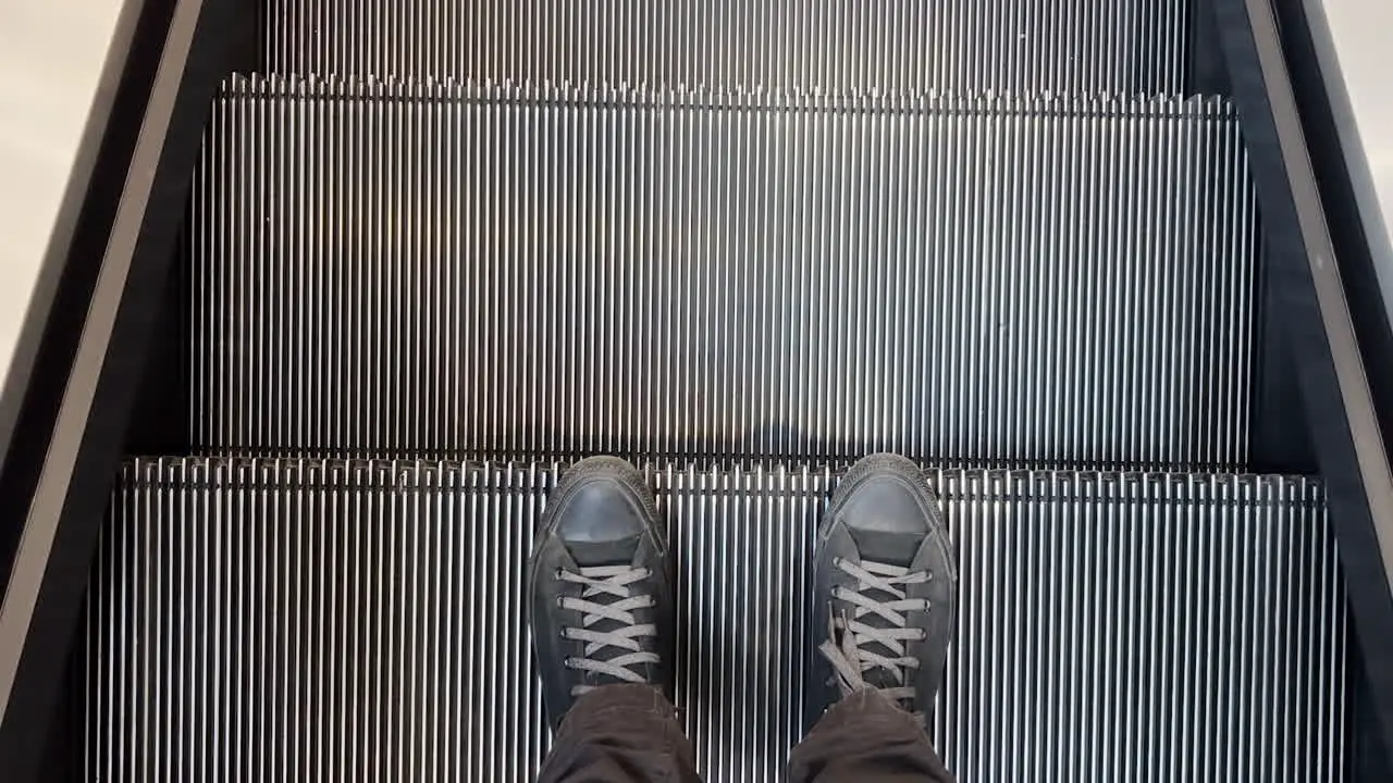 Male feet in black sneakers on escalator in shopping mall top view pov