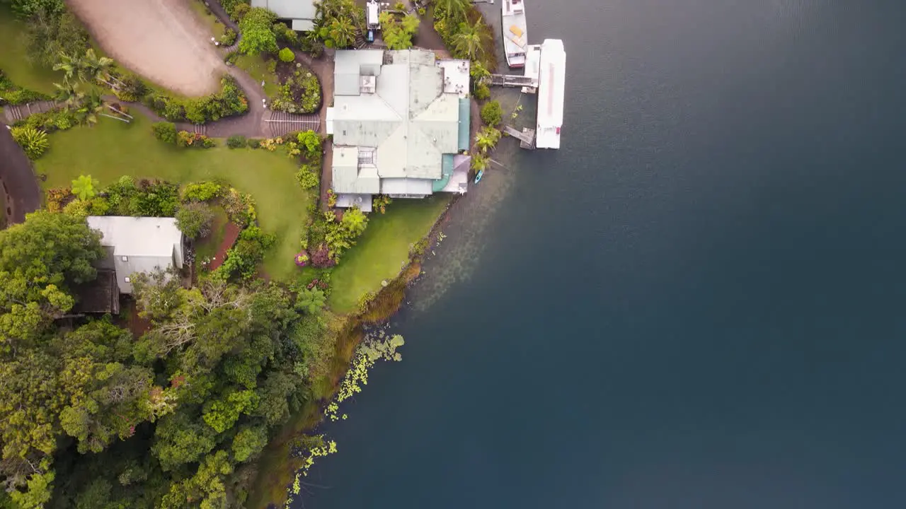 Moving drone video looking down on a lush park area next to a volcanic crater lake with boats docked next to pontoon