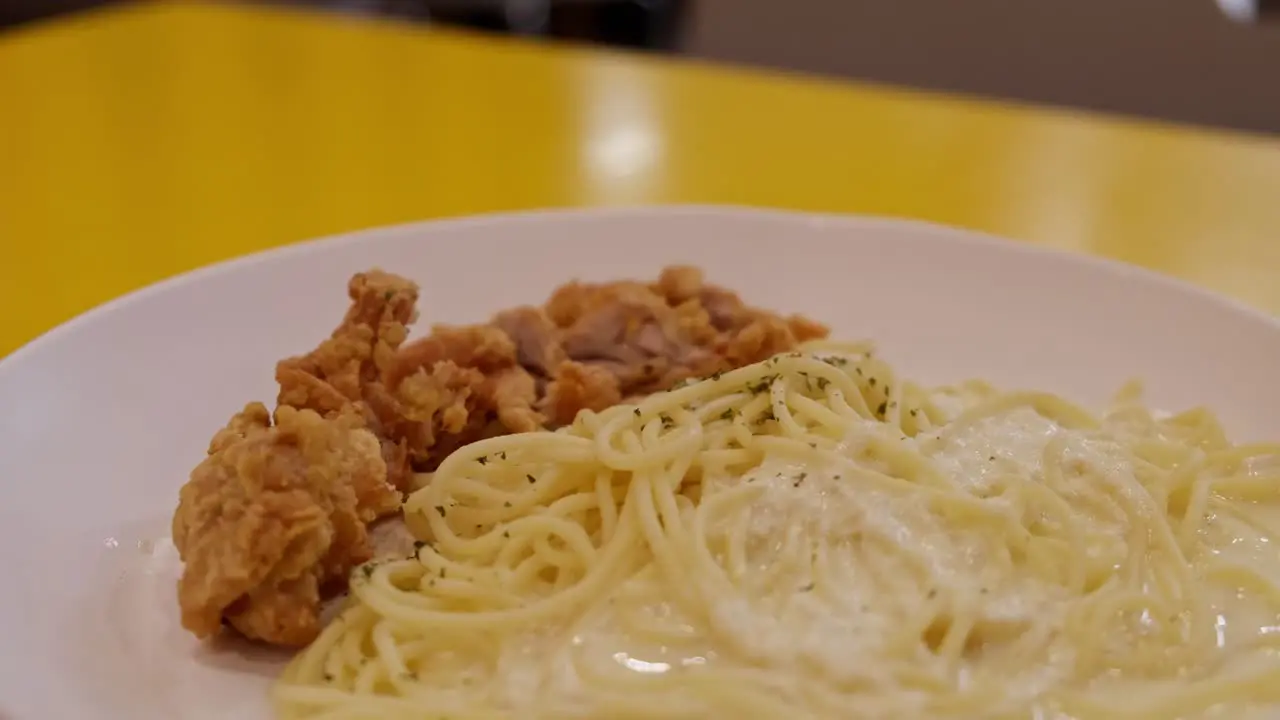 Pieces of fried chicken served with spaghetti with white sauce and some spices looks like a delicious Carbonara meal