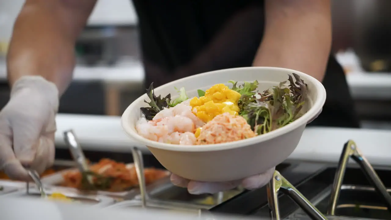 Worker scoops and adds chopped mango to poke bowl salad slow motion 4K