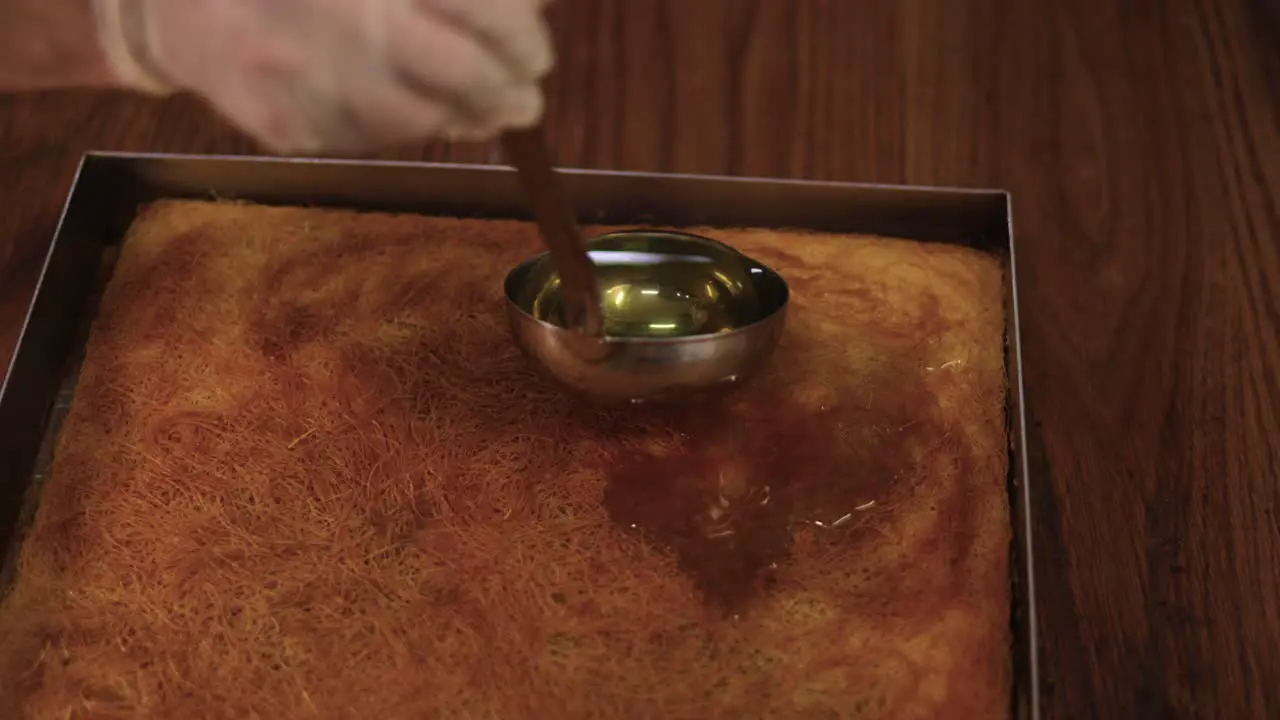 Pastry chef pouring the syrup over the dessert pan with cooking spoon