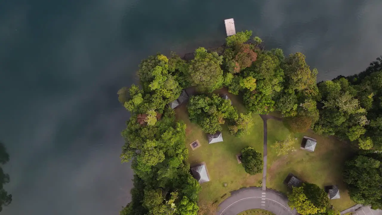 Static drone video looking down on a lush park area next to a volcanic crater lake with clouds reflecting on the calm water