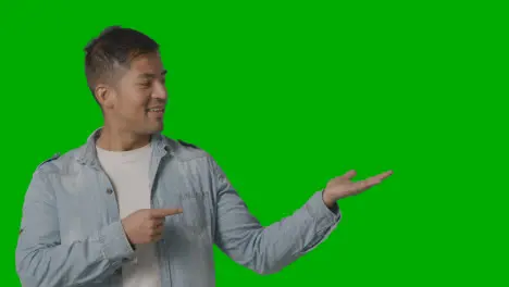 Studio Shot Of Casually Dressed Young Man Presenting Or Showing Against Green Screen 