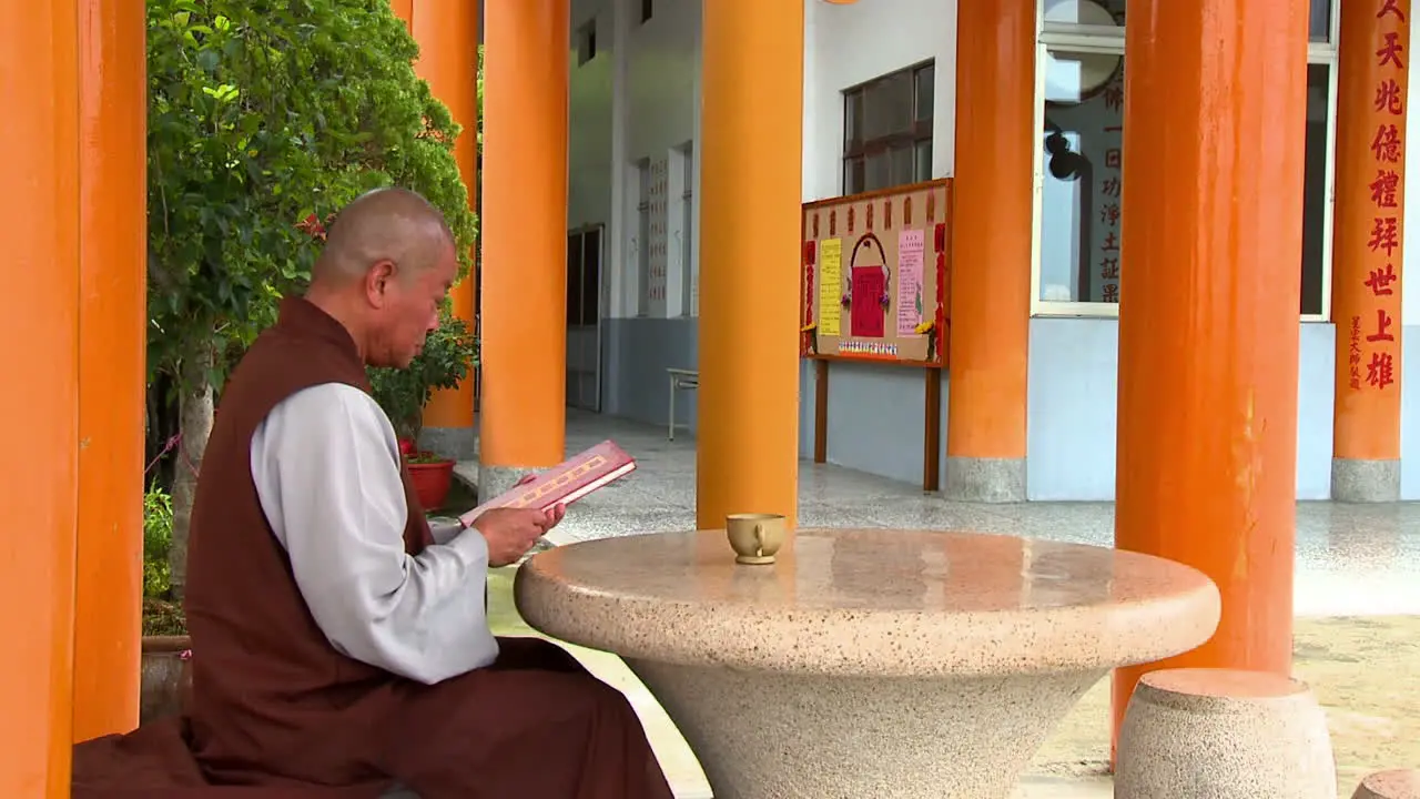 Monk in temple seated at round table looking at red book