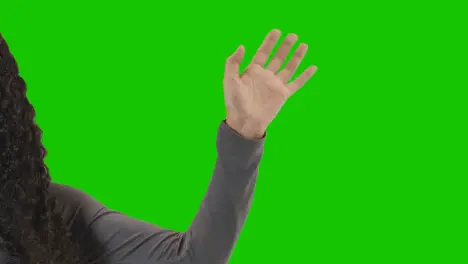 Studio Close Up Shot Of Woman Waving At Camera Against Green Screen