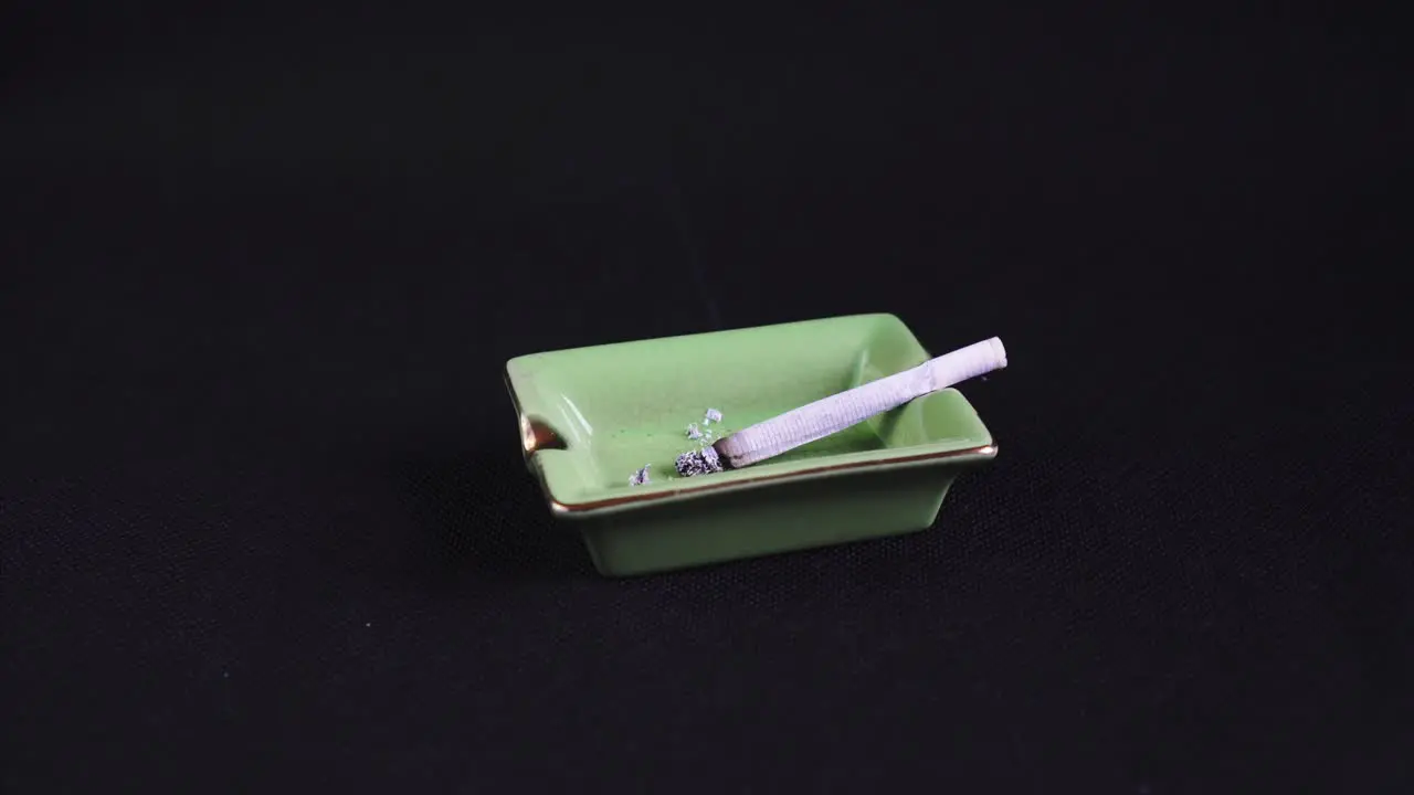 Rolled Cigarette or Joint burning out legalised marijuana on green Ashtray