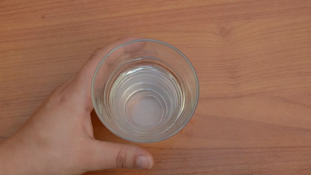 woman taking pink pills and putting glass of water back on the table