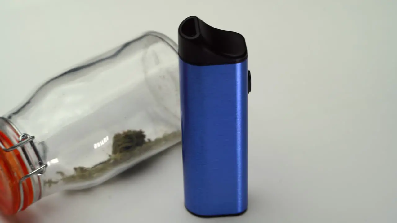 Slow reveal of a blue vaporizer next to a clear sealed jar of marijuana