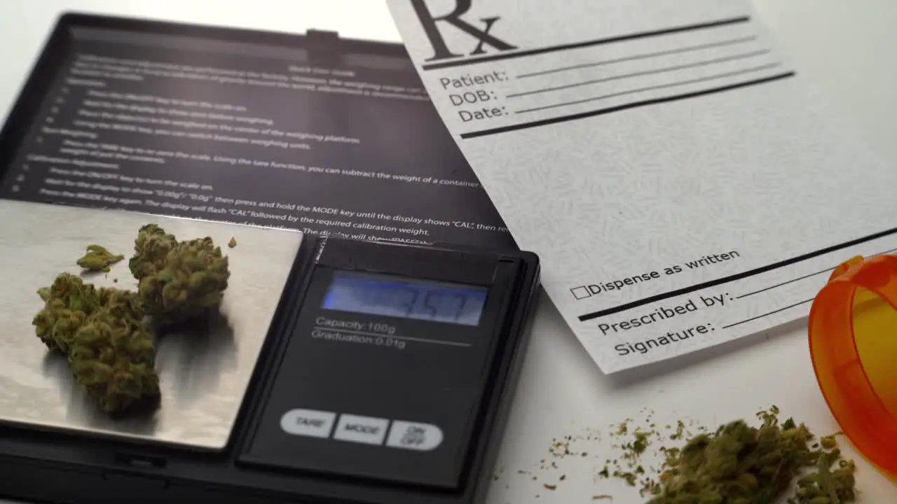 A digital scale measures grams of marijuana next to a prescription note and open pill bottle spilling a small pile of marijuana