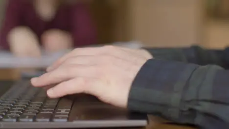 Sliding Close Up Shot of Hands Typing On Laptop with Child In Background Doing Homework