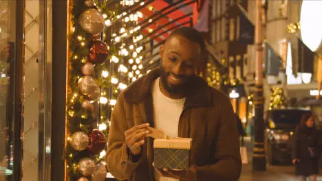 Man Walking Along Street On Christmas Shopping Trip To London Holding Present Or Gift