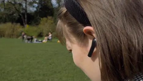 Close Up Shot of Young Woman Placing Earphone In Her Ear In Park