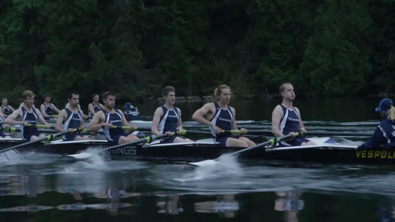 College athletes row on a calm lake as the camera pushes in cinematically