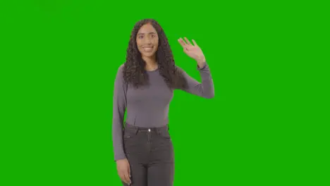 Studio Three Quarter Length Shot Of Woman Waving At Camera Against Green Screen