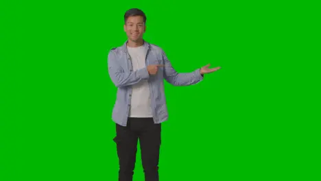 Three Quarter Length Studio Shot Of Casually Dressed Young Man Presenting Or Showing Against Green Screen 