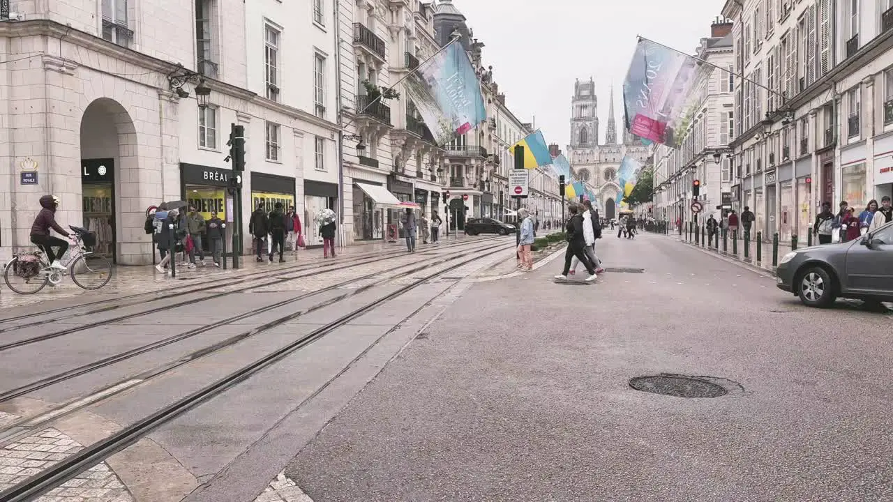 Crossing the street with tram tracks on a rainy day in Orleans France with other pedestrians