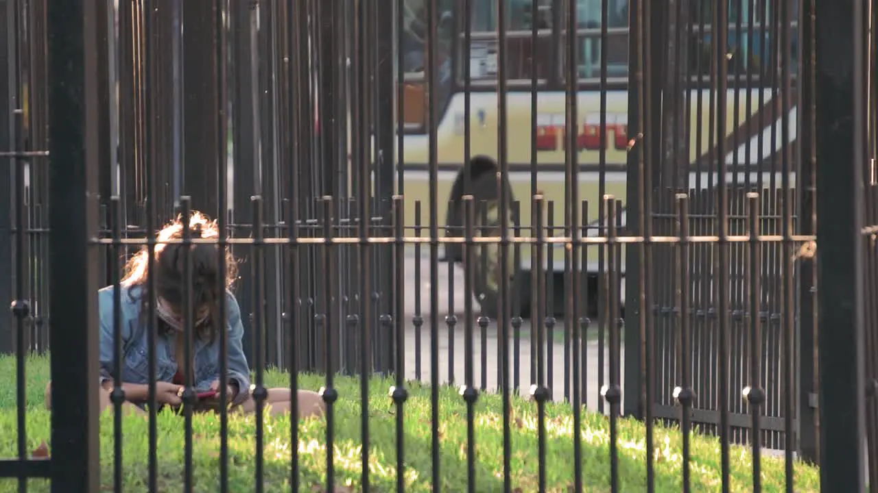 young girl wearing mask using phone in the park surrounded by fence