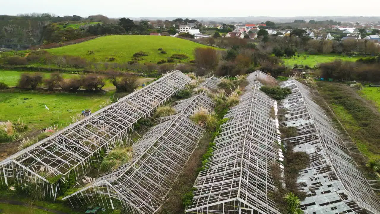 Flight over old derelict glasshouses in Guernsey across to green fields with houses in the background slow flight showing dereliction