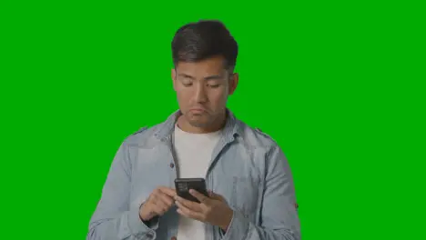 Studio Shot Of Casually Dressed Young Man Online Swiping On Mobile Phone Against Green Screen 1