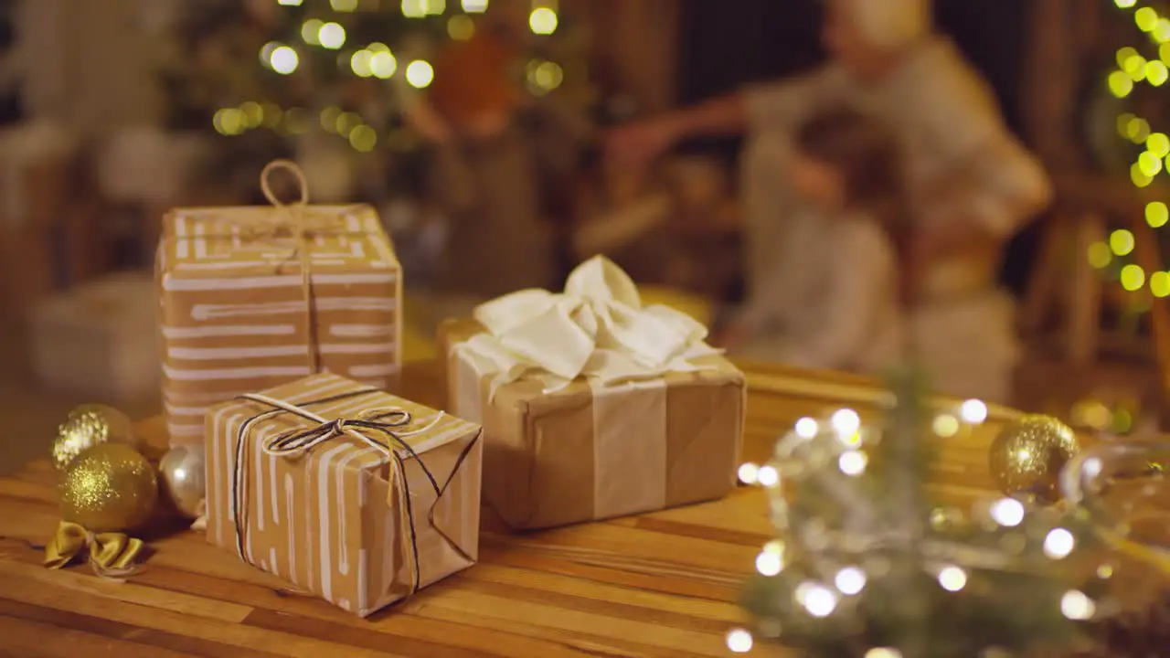 Close Up Of Christmas Gifts On A Table Grandmother Playing With Her Grandchildren On The Background