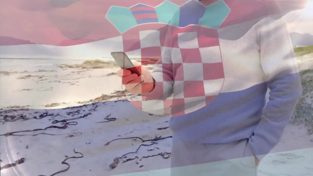 Animation of flag of croatia over senior caucasian man using smartphone on beach