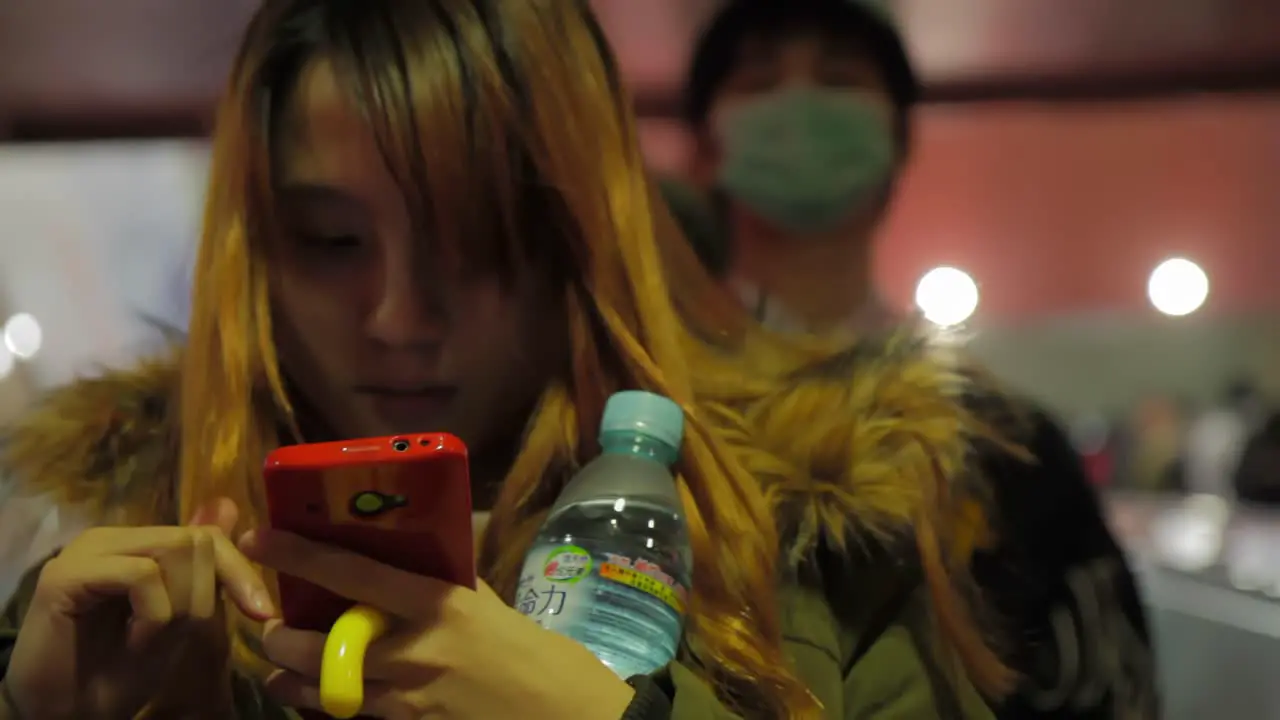 Asian girl with red phone and bottle of water in hand typing on escalator