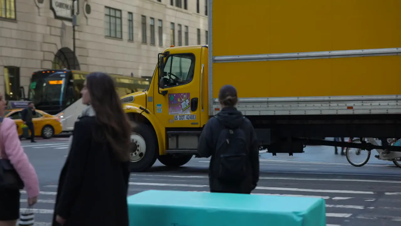 Slow-motion tracking shot of a yellow delivery truck crossing busy intersection in New York City USA