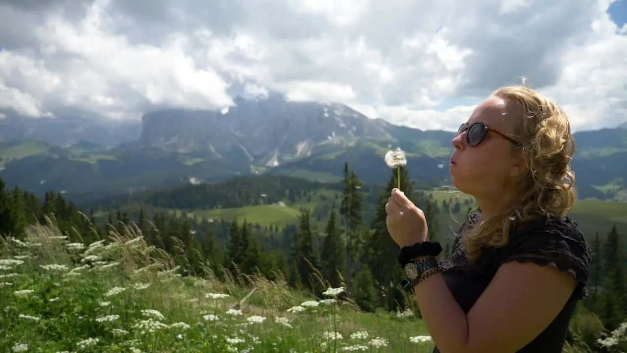 Super Slow Mo of a Blonde Girl blowing a dandelion flower in the wind in a beautiful nature setting outdoor in the summer Val gardena Alpe si Siussi