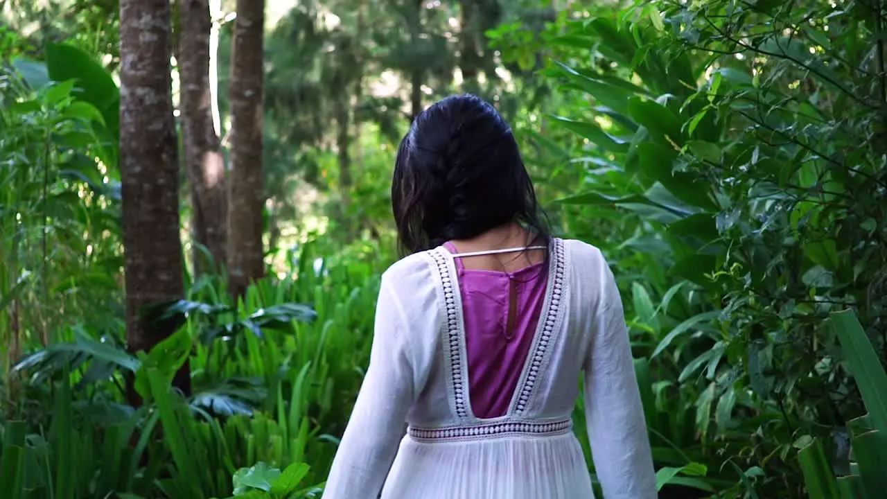 Following a woman walking into the forest while touching and caressing the lush vegetation and the green leaves