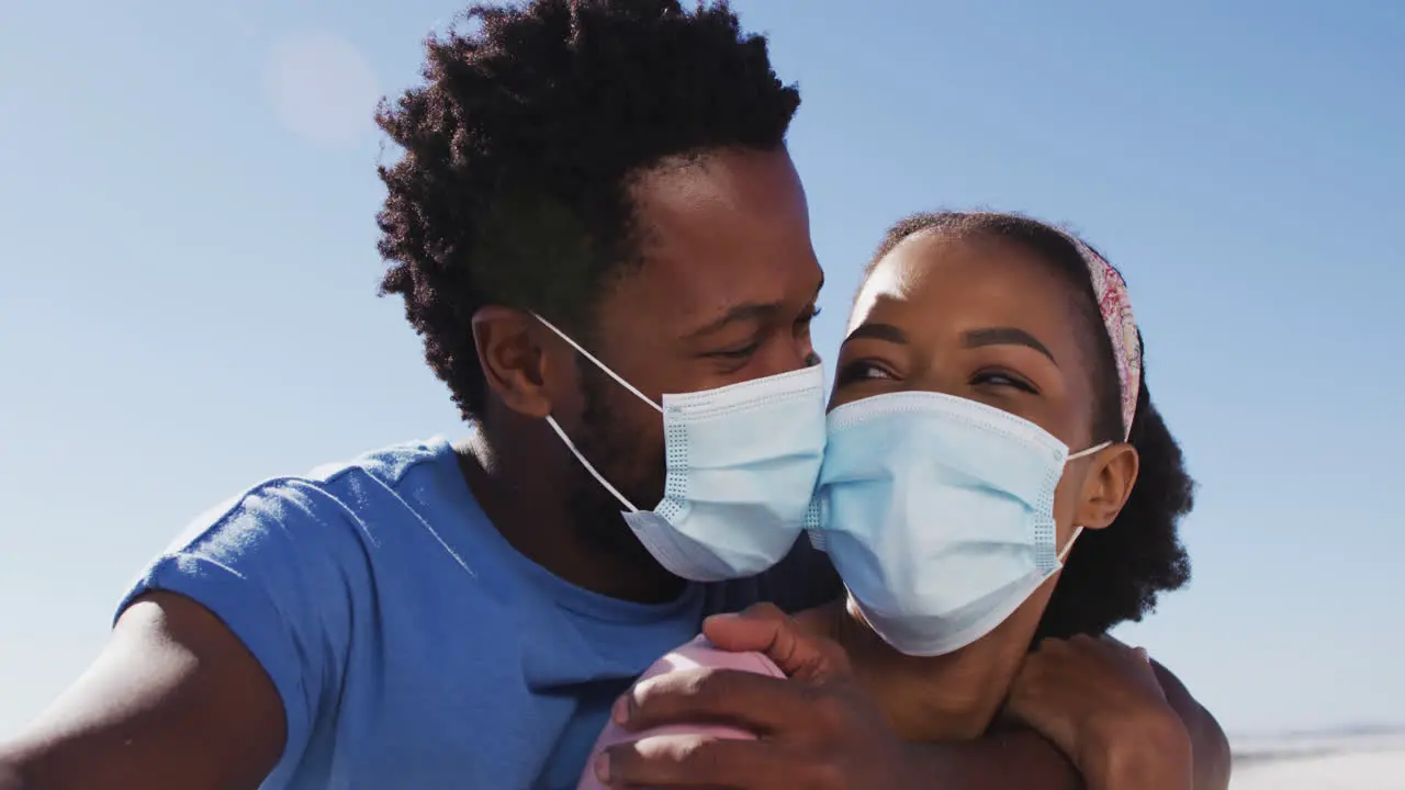 Portrait of african american couple wearing face masks looking to camera on the beach