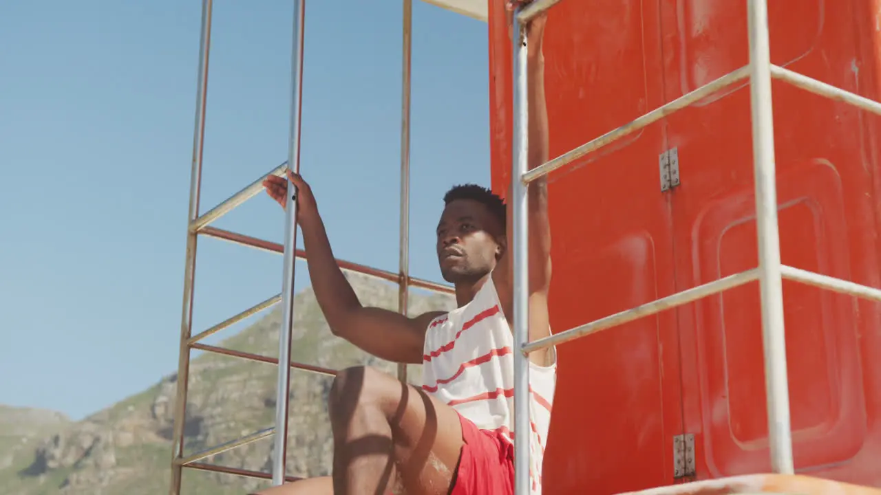 African american male lifeguard inspecting on tower on sunny beach