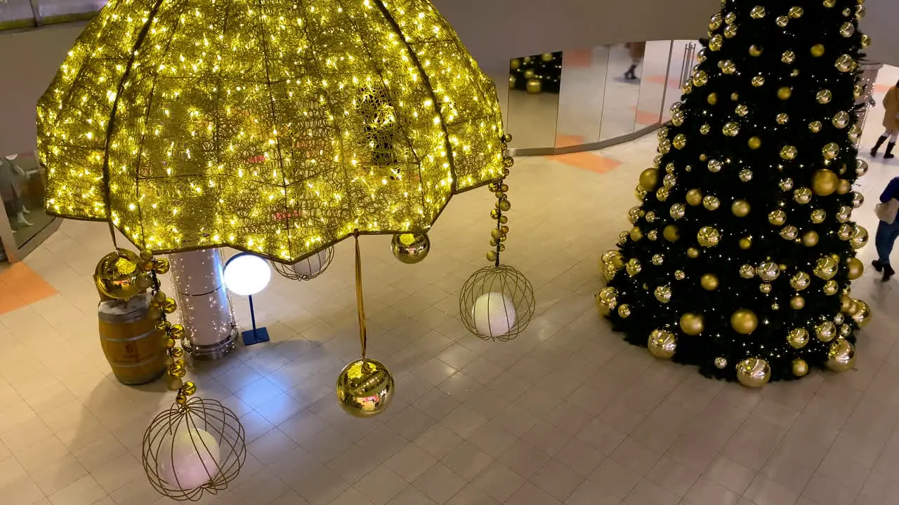 Big Christmas Tree decorated with golden balls in a shopping mall people walking on background wearing masks