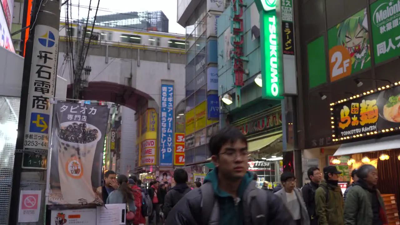 Street level view of sbusy street in Akihabara Tokyo with train running on tracks above