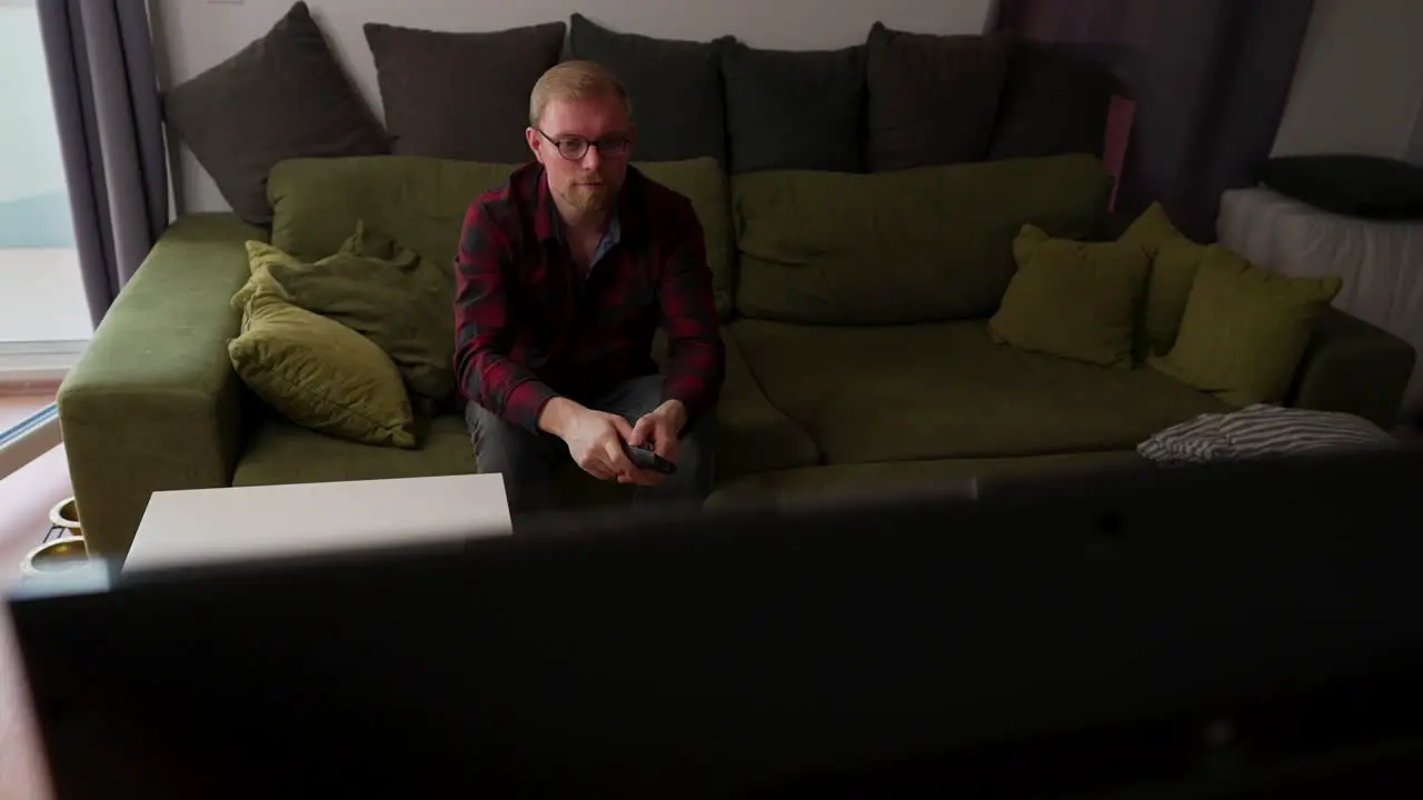 Caucasian Man with Beard Sits on Couch Uses Remote Controller Casual Day Home