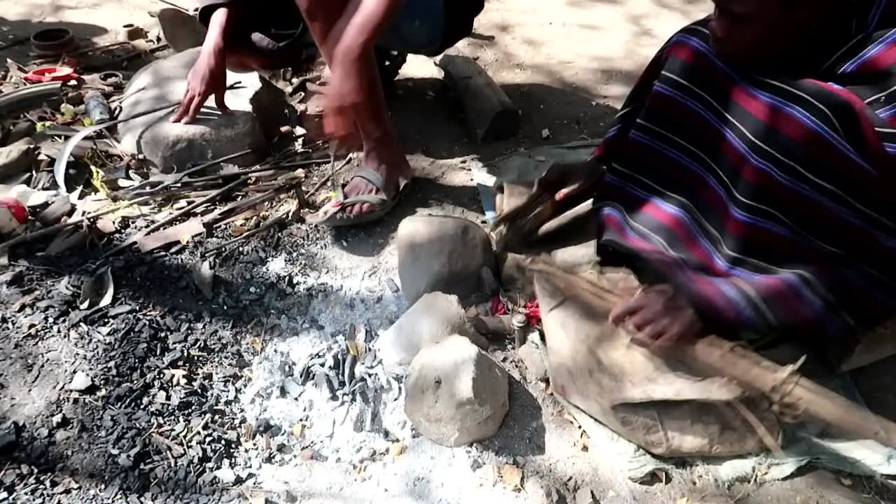 Datoga tribe man blowing embers with a rudimental handmade system to melt metal