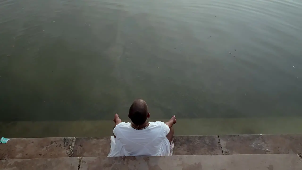 A man is sitting on the edge of a river with his feet in the water