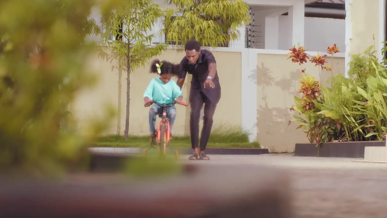 African father assisting her daughter to learn how to ride bicycle at home