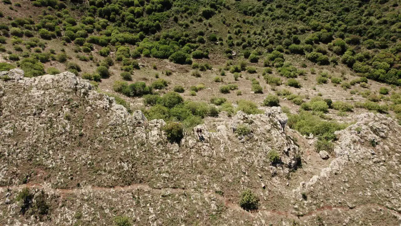 drone flying backwards with the camera tilting up filming 2 persons standing on the edge of a large crater in 4k