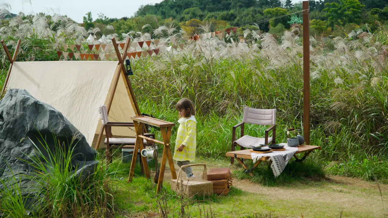 Blond Child Girl at Summer Camping Site in Nature Explore Kitchen Utensils by Old Style Tent Ecorium Botanical Garden wide slow motion