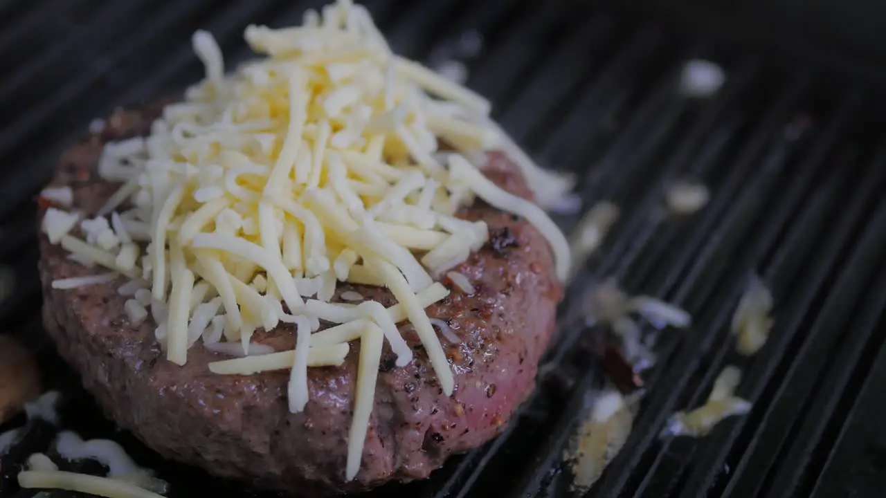 One hamburger patty frying on medium heat in a cast iron grill skillet