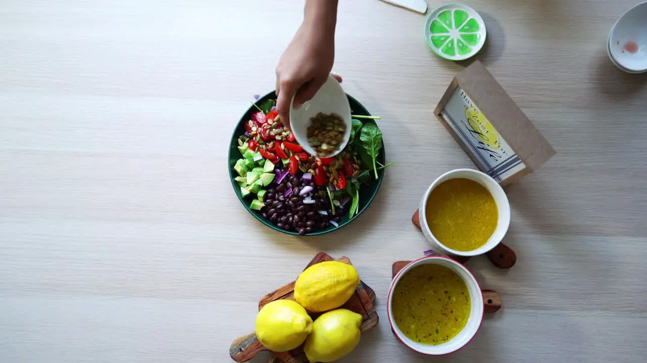 Assembling salad aerial shot of salad on platform black beans lemons pumpkin seeds avocado tomatoes leaf spinach dressing